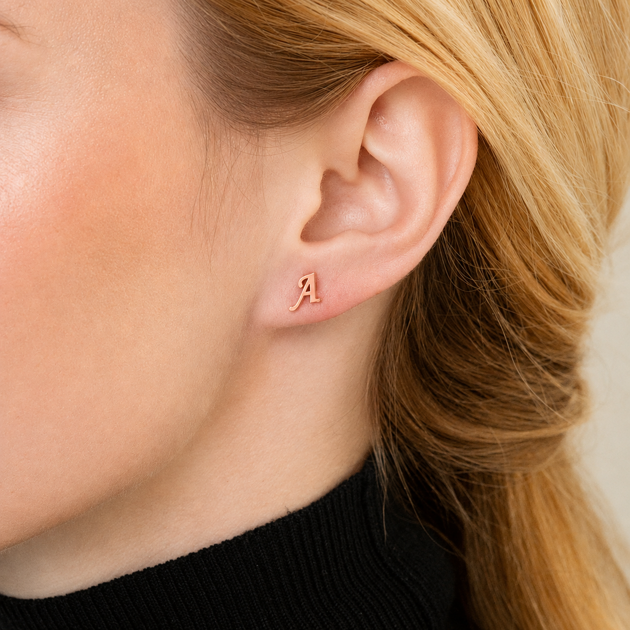 Close-up of a person wearing a gold earring with the letter 'A' on a neutral background